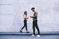 Male and female hipsters walking on grey wall background ignoring each other preferring social netwo...
