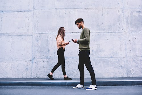 Male and female hipsters walking on grey wall background ignoring each other preferring social netwo...