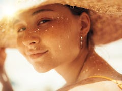 Mysterious young woman look with attraction on camera and pose. Hold straw hat with one hand. Sit ou...