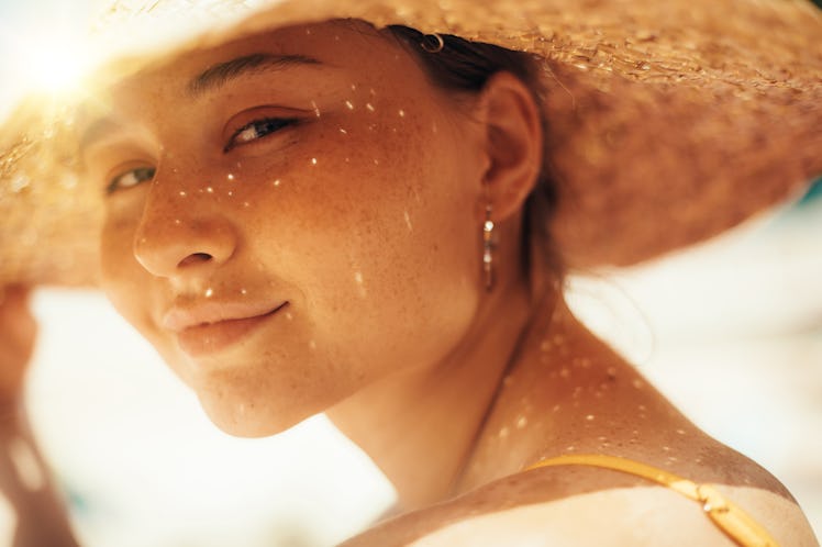Mysterious young woman look with attraction on camera and pose. Hold straw hat with one hand. Sit ou...