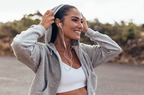 Fitness woman wearing a hooded shirt walking outdoors. Smiling female on early morning walk.