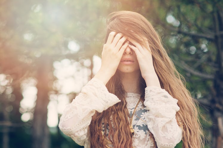 Shy or emotional woman with long blonde hair outdoors in forest on sunny day. Matte filter, back lig...