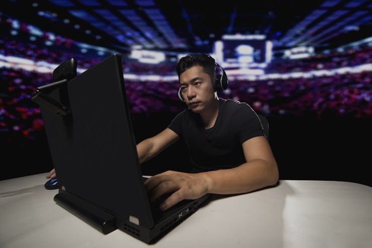 Competitive asian male professional E Sports video gamer playing an FPS, or MMO game on a computer a...