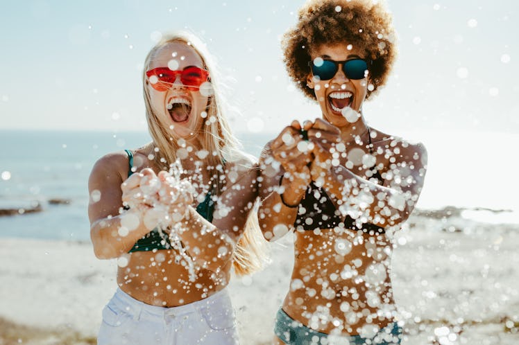Excited young women friends bursting a water balloon and smiling by the sea. Best friends having fun...