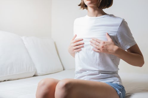 Woman sits on a bed and holds her breasts. These common areola changes can help explain why your nip...