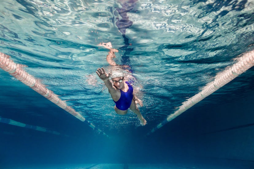 underwater picture of female swimmer in swimming suit and goggles training in swimming pool