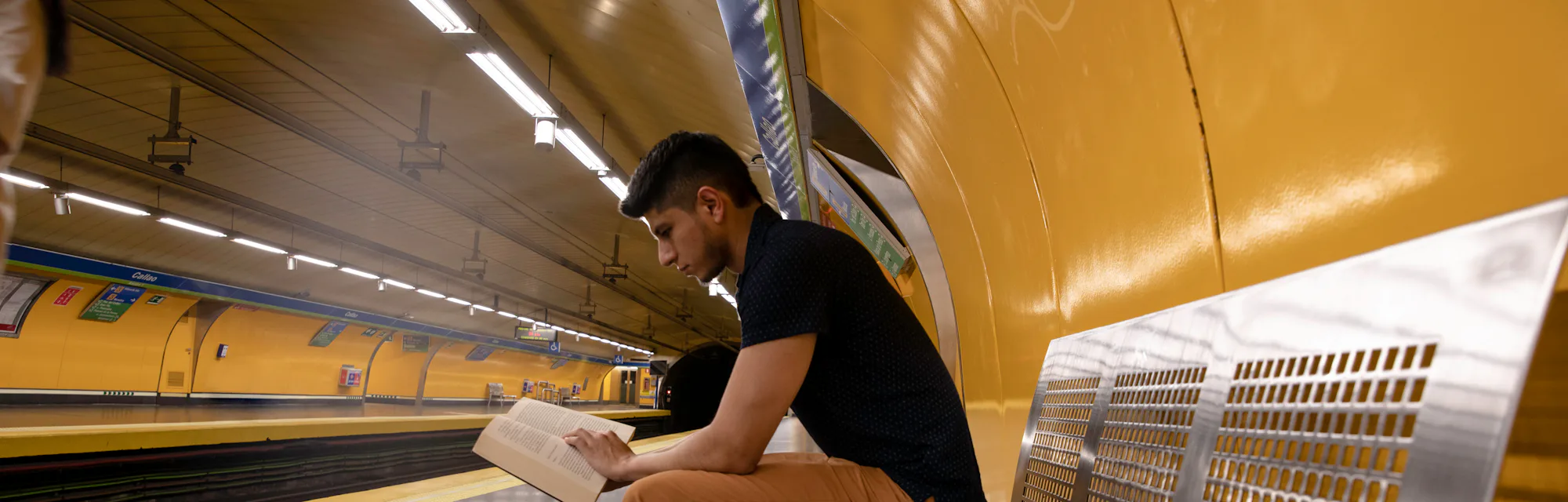 young man reading a book while waiting for the subway at the station