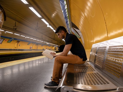 young man reading a book while waiting for the subway at the station