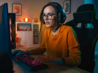 Upphetsad Gamer Girl i headset med ett mikrofon som spelar onlinespel på sin persondator. Hon tal