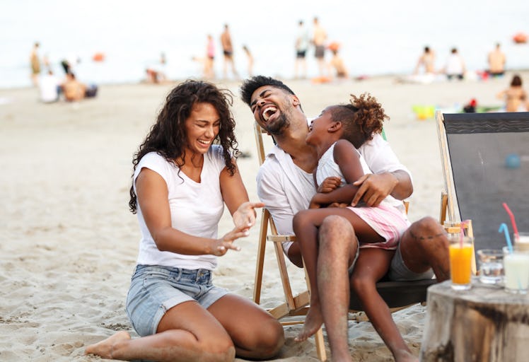 A mom, dad, and daughter laugh while spending time at the beach.