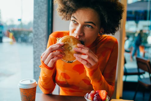 A woman eats a hamburger on a bagel. Wondering why meat makes you feel sick? Some people have stomac...