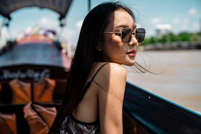 attractive female traveler wearing sunglasses look away while traveling on traditional long tail boa...