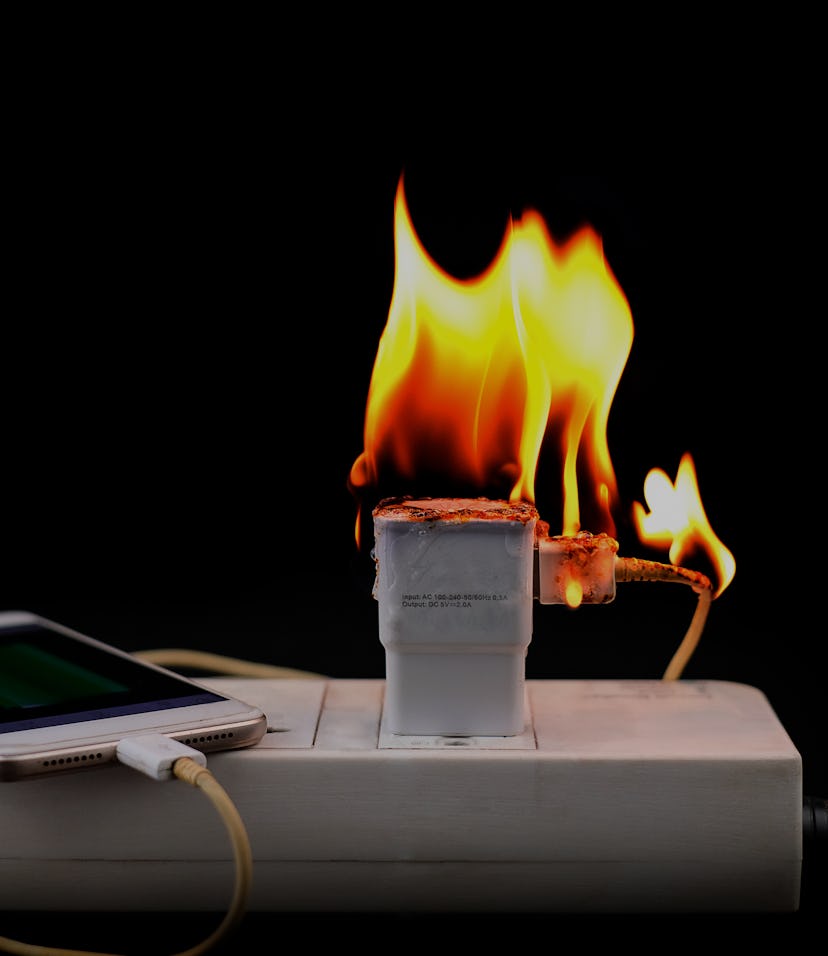 On fire Adapter smart phone charger at plug in power outlet at black background