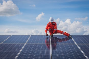 A construction worker building solar panels against a blue sky.
