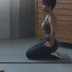 A person with natural, curly hair kneels on a yoga mat during a stretch routine. Working out with de...