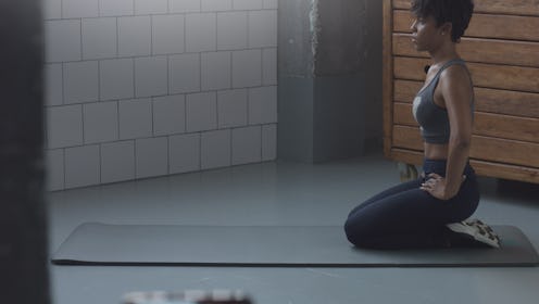 A person with natural, curly hair kneels on a yoga mat during a stretch routine. Working out with de...