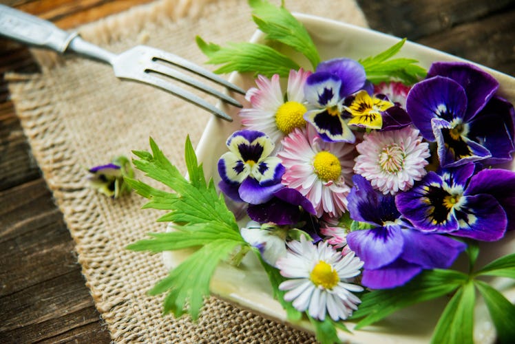A plate filled with edible flowers sits on a table with a fork resting against it. 