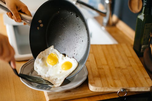 Two fried eggs in a pan with olive oil. Girl's hand holding a frying pan with scrambled eggs.