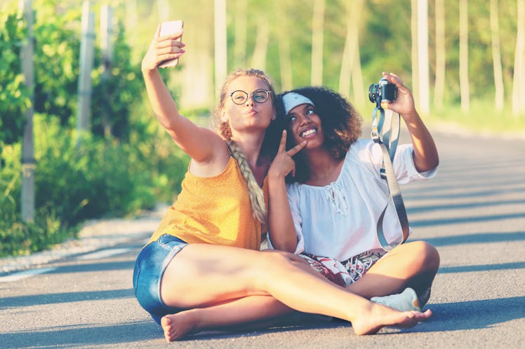 Female friendship concept with multiethnic girls couple taking selfie outdoors in countryside road -...