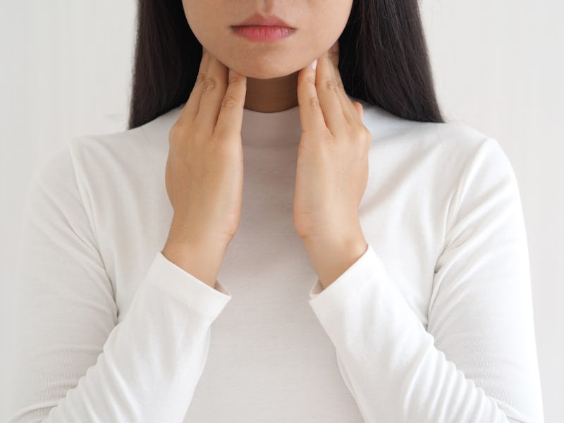 A woman holds her hands up to her throat, monitoring her sore throat for symptoms of coronavirus.