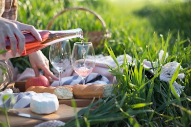 Summer - Provencal picnic in the meadow.  girl pouring wine into glasses near a picnic basket and ba...