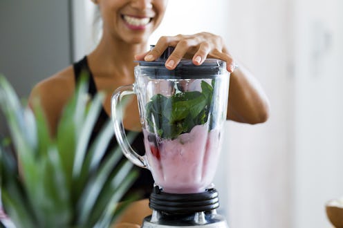 Woman blending spinach, berries, bananas and almond milk to make a healthy green smoothie