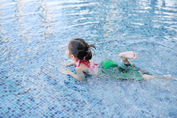 Little Asian child girl wear mermaid swimming suit has fun at the pool.