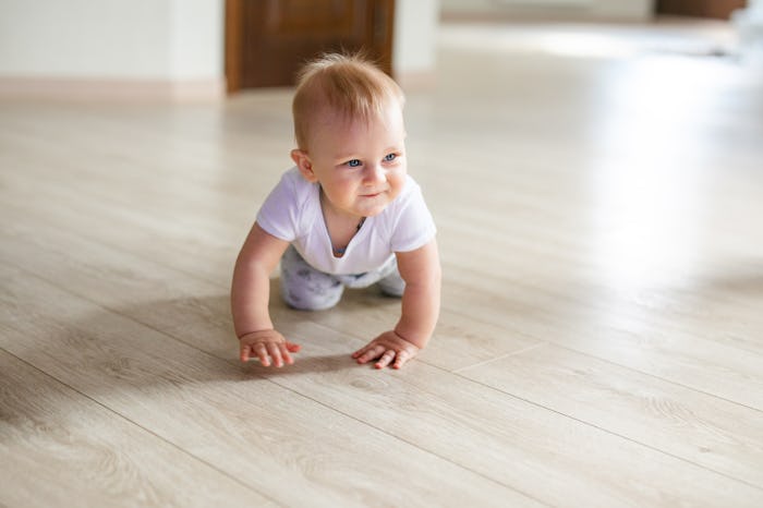 Cute little baby boy lying on hardwood and smiling. Child crawling over wooden parquet and looking u...