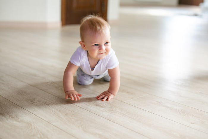 Cute little baby boy lying on hardwood and smiling. Child crawling over wooden parquet and looking u...