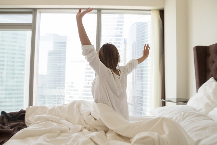 Rear view at woman sitting on bed stretching awaking after sleeping well in the good weekend morning...