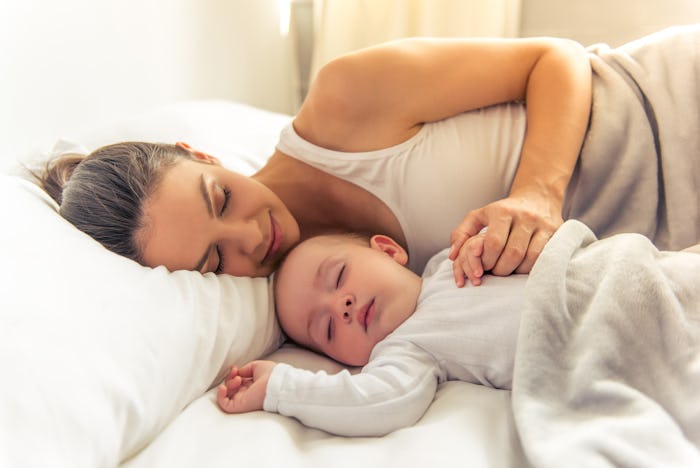 Side view of beautiful young mom and her cute little baby sleeping in bed at home