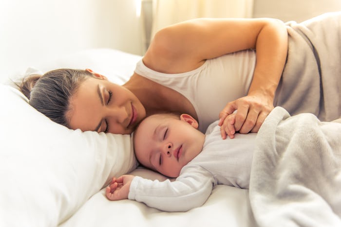 Side view of beautiful young mom and her cute little baby sleeping in bed at home