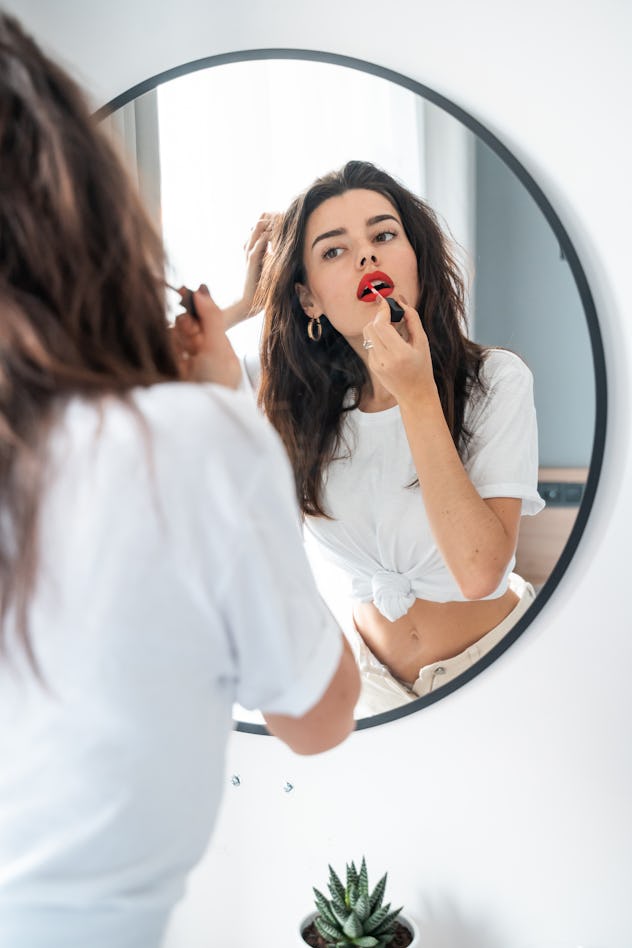 Young woman applying lipstick looking at mirror