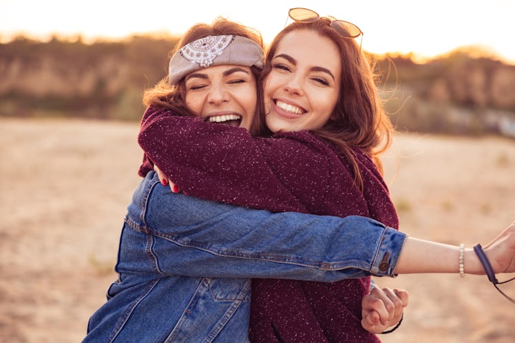 Image of happy young caucasian friends ladies walking outdoors on the beach hugging.