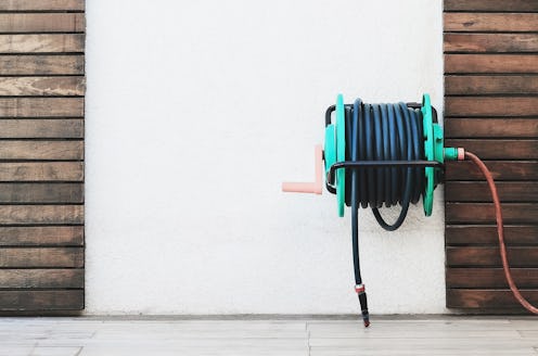 Background of a garden hose reel fixed on the wall. Blank wall on center with wooden boards decorati...