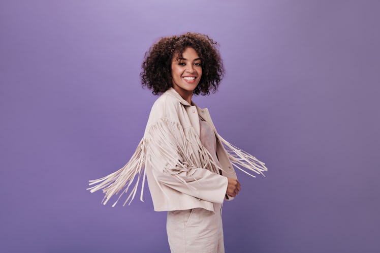 Attractive woman in jacket with fringe whirls on isolated background. Portrait of young brunette gir...