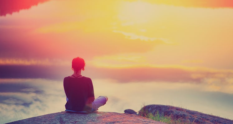 Young woman sitting enjoying peaceful moment of beautiful colorful sunset. In the reflection of the ...