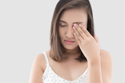 Asian woman suffering from strong eye pain against a gray background. Female has a pain in the eye. ...