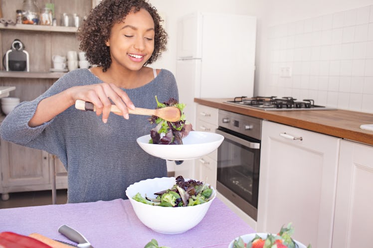 Portrait of beautiful african american adolescent girl serving salad, eating fruit and vegetables in...