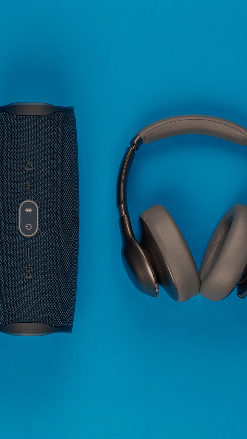 A pair of headphones next to a black speaker on blue background, shot from above.
