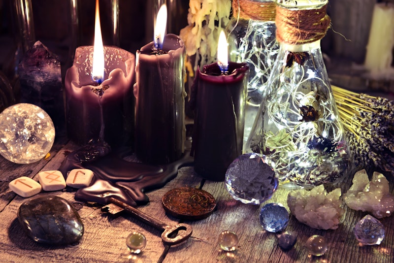 Magic crystals, ritual objects, runes, black candles and bottles on witch table. Occult, esoteric and divination concept. 