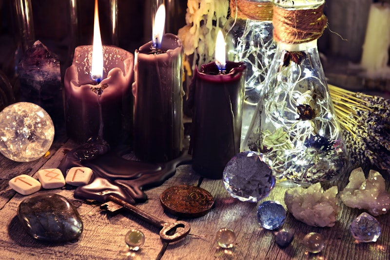Magic crystals, ritual objects, runes, black candles and bottles on witch table. Occult, esoteric and divination concept.
