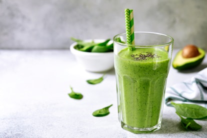 Green detox smoothie from avocado and baby spinach in a tall glass on a light grey slate, stone or c...