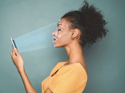 Woman scanning face with facial recognition system on smartphone, with rays coming out of the phone ...