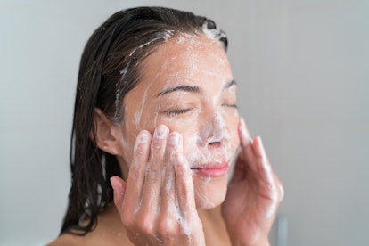 Skincare woman washing face in shower foaming facewash soap scrub on skin. Asian female adult cleani...