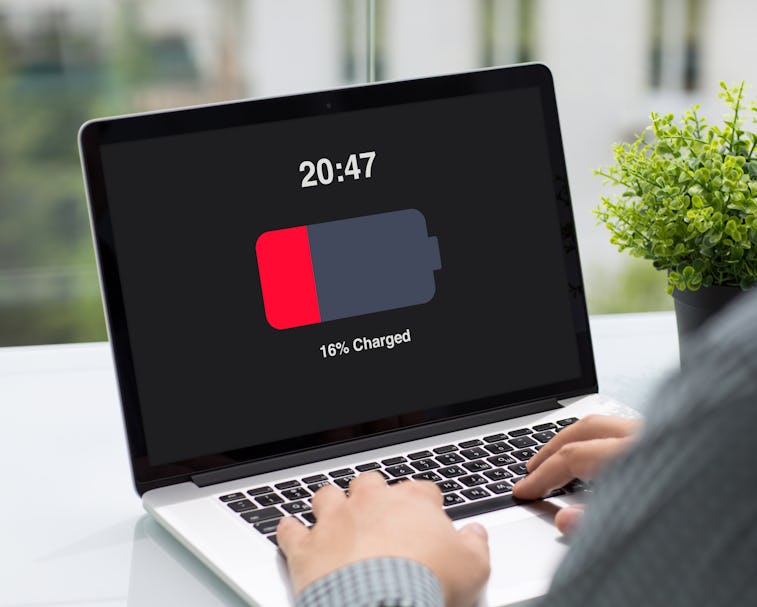 Man holding computer with low charged battery screen on table in cafe