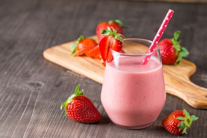 Glass of fresh strawberry milkshake, smoothie and fresh strawberries on pink, white and wooden backg...