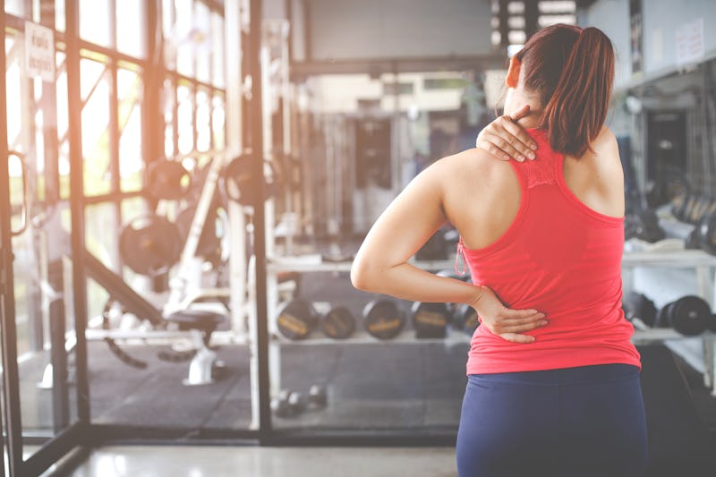 A person wearing a red workout shirt faces away from the camera, rubbing at a sore spot in their nec...