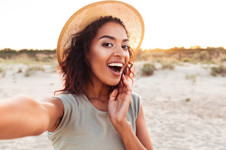 Close up of cheerful young african girl in summer hat taking a selfie at the beach