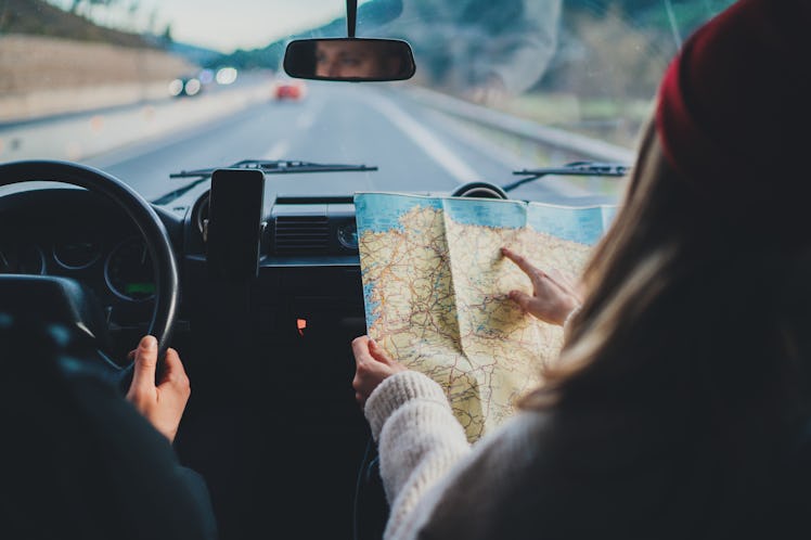 Happy couple traveling by authentic car in Europe, hipster girl holding touristic map planning route...